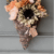 Fall floral grapevine wreath basket door decor hanging on a sage green front door with pretty fall flowers, a sweater pumpkin pick and a hangtag that says "Fall vibes".