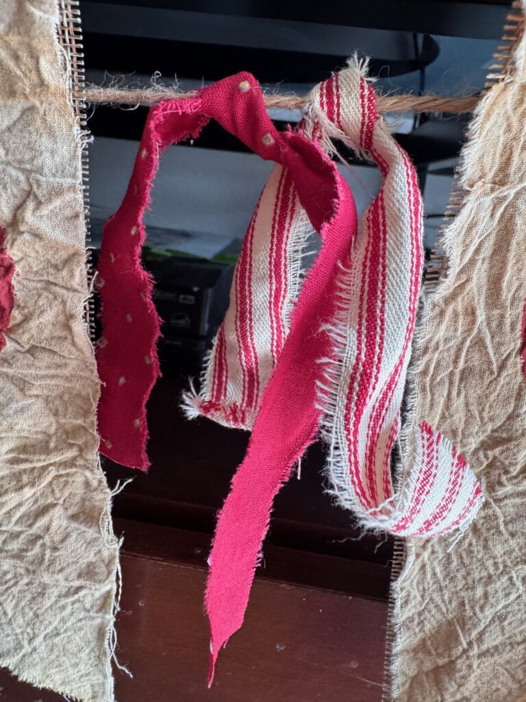 2 pieces of fabric tied to the twine garland, one red and one red and white homespun.
